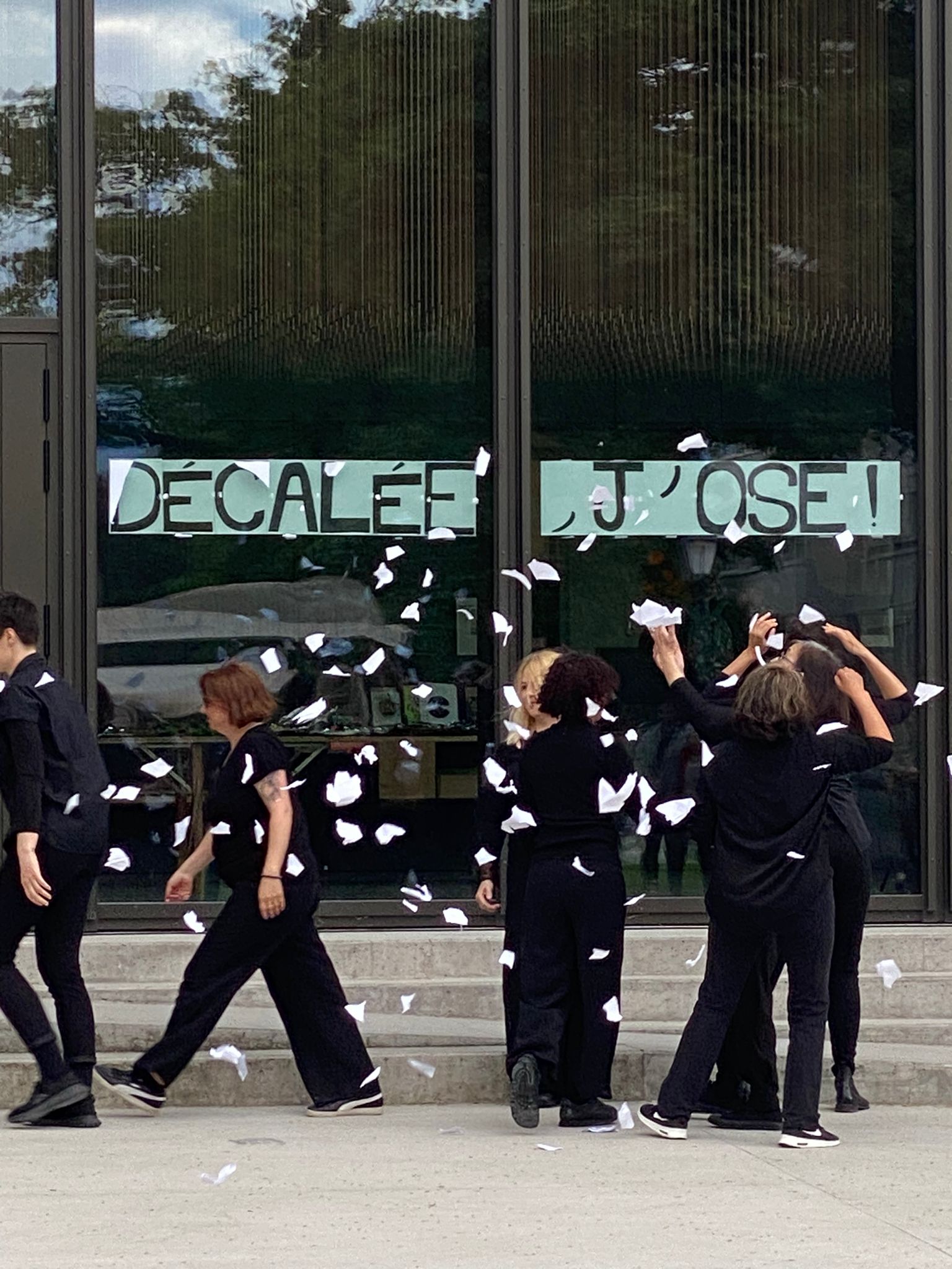 Femmes lançant des papiers déchirés en l'air devant la façade de l'ADC où il est écrit "Décalée, j'ose"